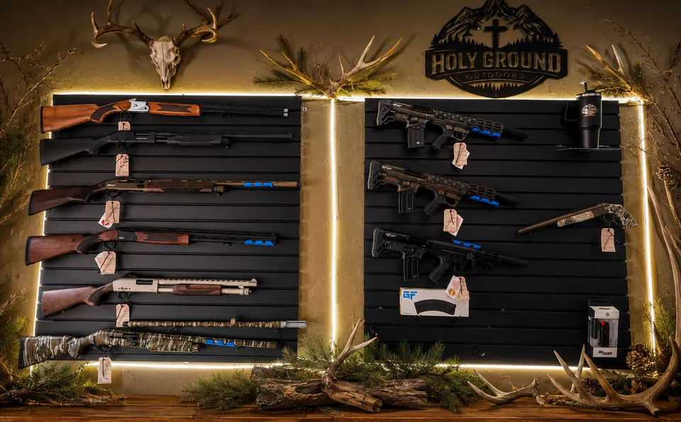 Shotguns and tactical firearms on the Holy Ground Outdoors display wall