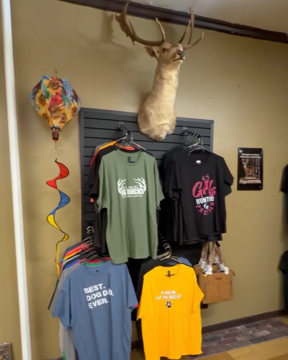 Hunting and faith graphic t-shirts displayed beneath a mounted whitetail buck
