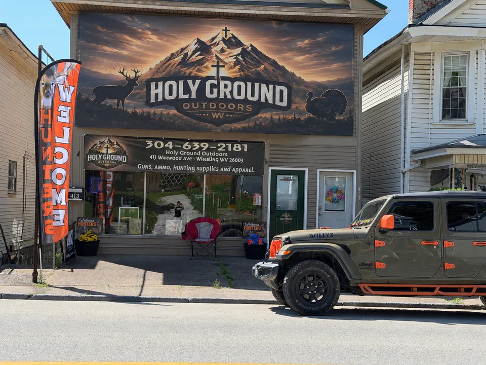 Holy Ground Outdoors storefront on Warwood Avenue in Wheeling, West Virginia, with its mountain-and-cross mural and Welcome flag