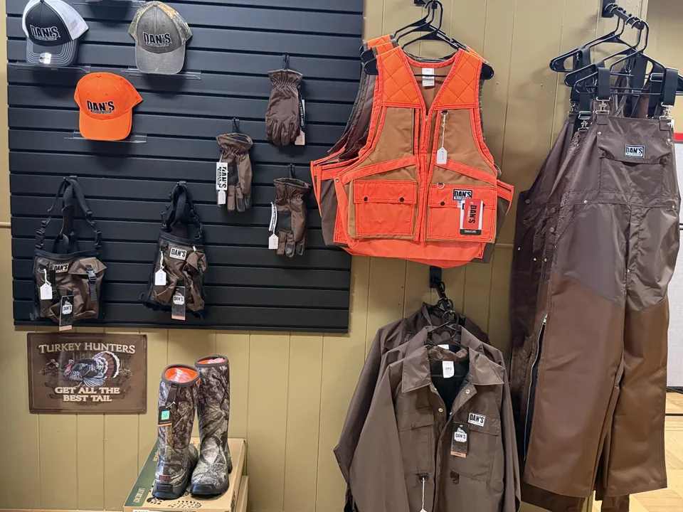 Dan's Hunting Gear apparel display — briar-proof vest, bibs, gloves, caps, and snake boots